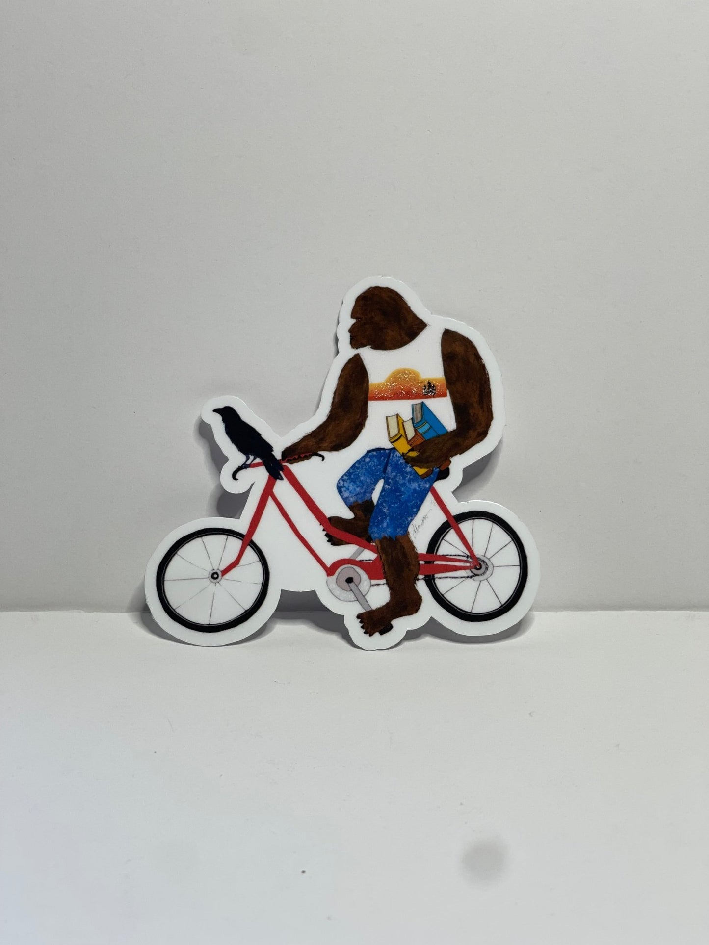 Bigfoot with books on bike with Crow – Whimsical Sasquatch Vinyl Decal Die Cut Sticker - Color Crumbs Club