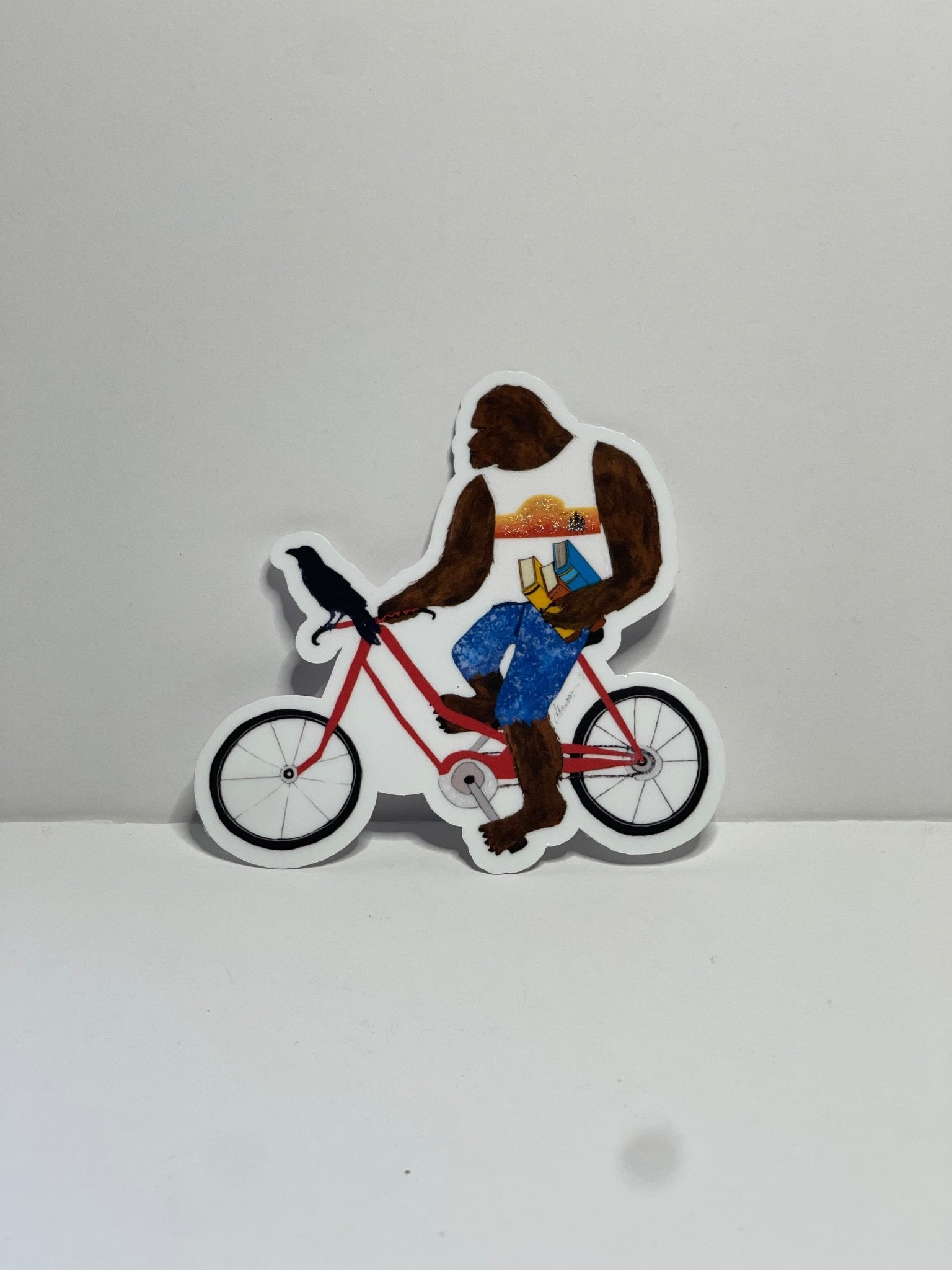 Bigfoot with books on bike with Crow – Whimsical Sasquatch Vinyl Decal Die Cut Sticker - Color Crumbs Club